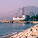 Industrial plant by the sea with mountain backdrop and rocky shore. Ideal for environmental and industrial themes.