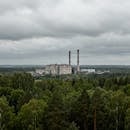 Aerial view of a large factory with smokestacks surrounded by dense forest under a cloudy sky.